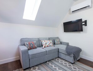 A grey sectional sofa with patterned cushions, a flat-screen TV mounted on the wall, and a patterned rug on the floor.