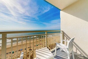Ein Balkon mit Blick auf den Strand, weißen Stühlen und einem Tisch.