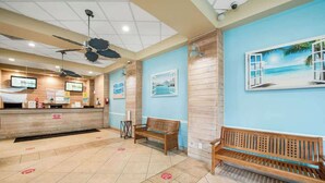 A reception area with a counter, wooden benches, ceiling fans, and wall art depicting tropical scenes. - Carolinian Beach Resort 1030 (Myrtle Beach)