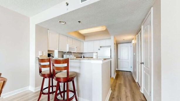 A modern kitchen with white cabinetry, a central island, and two bar stools. - Carolinian Beach Resort 1030 (Myrtle Beach)