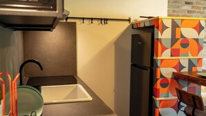 A compact kitchen with a black refrigerator, a small sink, and a dining area with a chair.