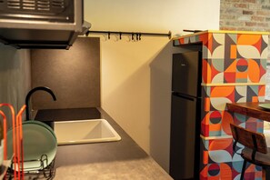 A compact kitchen with a black refrigerator, a small sink, and a dining area with a chair.
