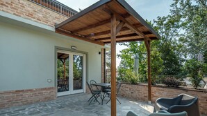 A covered patio with stone flooring, a table with chairs, and a wooden pergola structure.