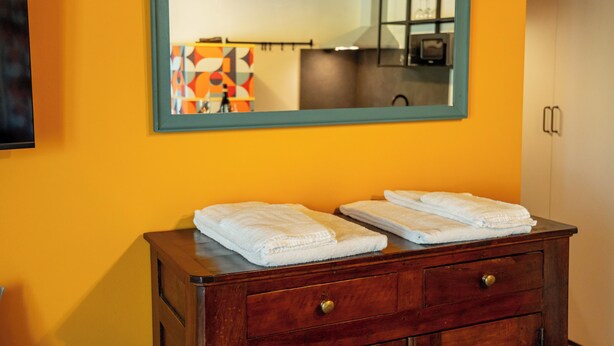 A bathroom with a wooden vanity, two folded white towels, a mirror with a teal frame, and a wall-mounted television.