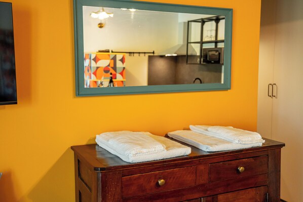 A bathroom with a wooden vanity, two folded white towels, a mirror with a teal frame, and a wall-mounted television.