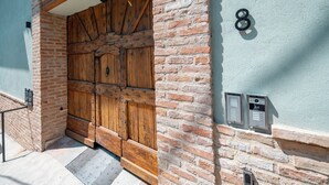 A large wooden door with metal reinforcements, a brick wall, and a numbered mailbox.