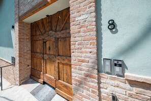 A large wooden door with metal reinforcements, a brick wall, and a numbered mailbox.