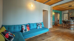 A cozy living area with a teal sofa, wooden flooring, and a kitchen area with a bar.