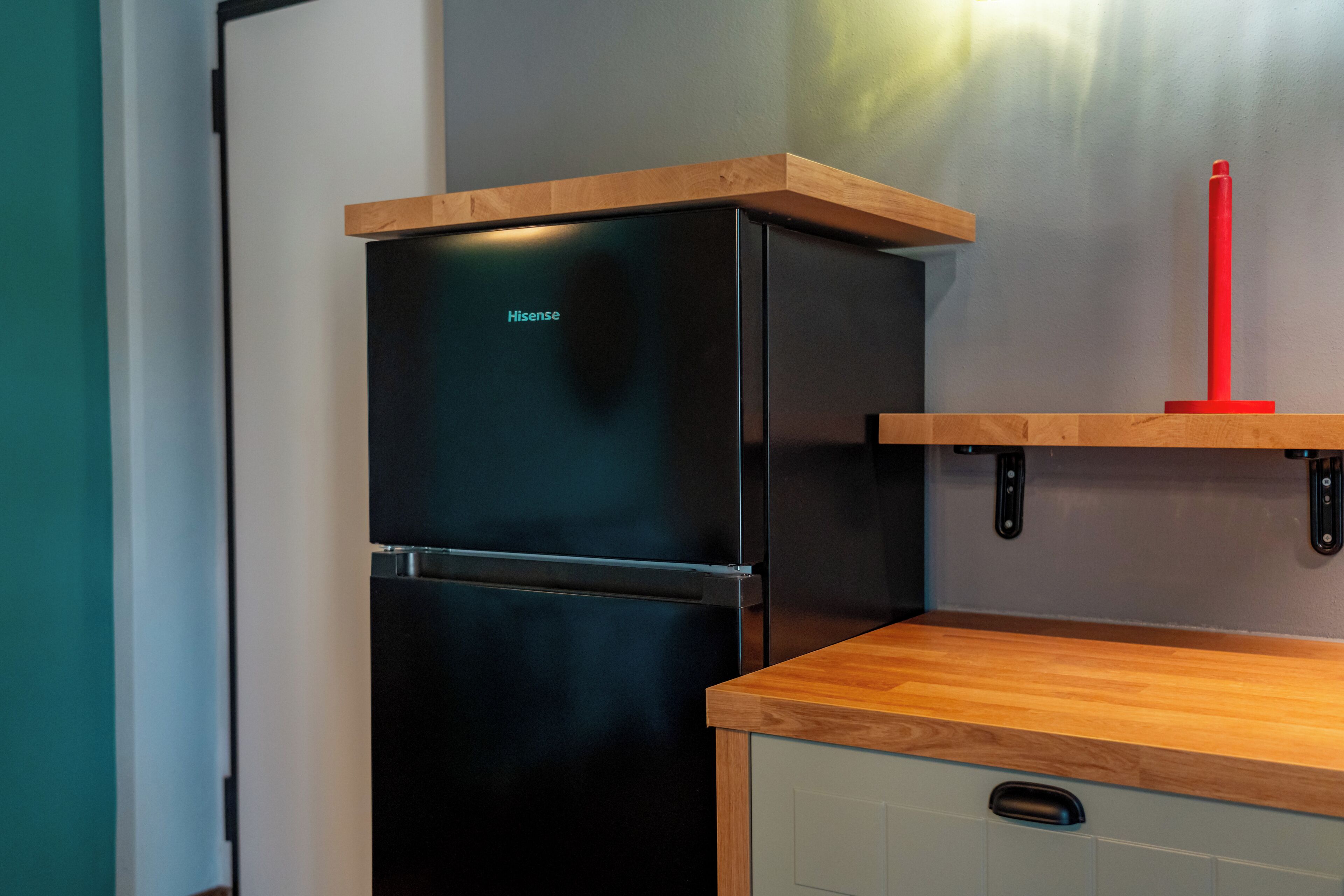 Una cocina con un refrigerador negro, encimera de madera y un portalapices rojo.