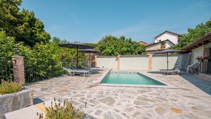 A stone pool with lounge chairs and umbrellas, surrounded by a garden and a brick wall.