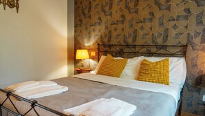 A neatly made bed with pillows and folded towels, a bedside lamp, and a patterned wallpaper.