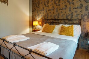 A neatly made bed with pillows and folded towels, a bedside lamp, and a patterned wallpaper.