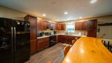 A modern kitchen with wooden cabinets, a black refrigerator, and a wooden dining table.