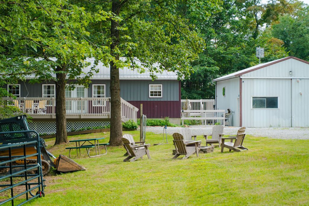A grassy area with picnic tables and chairs, a fenced deck, and a building with a red and white exterior.