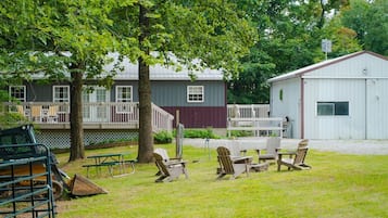 A grassy area with picnic tables and chairs, a fenced deck, and a building with a red and white exterior.
