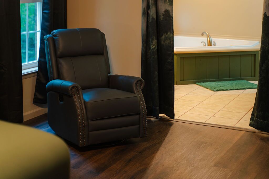 A room with a black leather chair, a wooden floor, a green mat, and a bathtub.