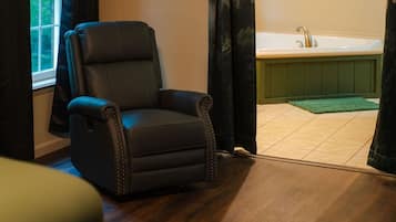 A room with a black leather chair, a wooden floor, a green mat, and a bathtub.
