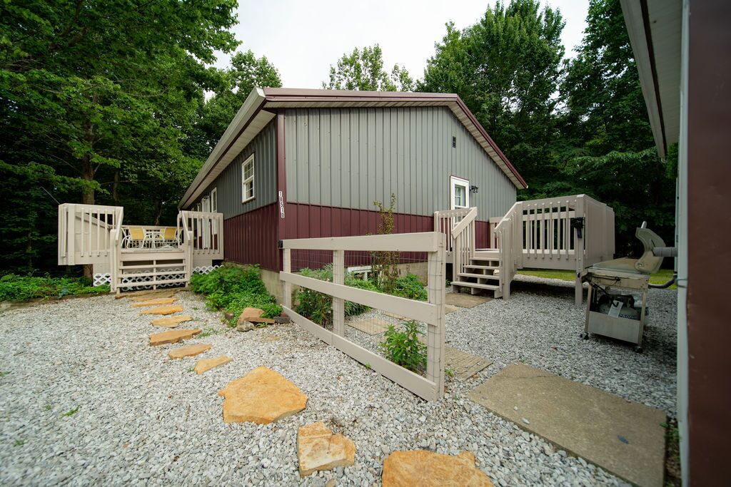 Un bâtiment de style rustique, évoquant une grange, avec une allée en gravier et des portails en bois.