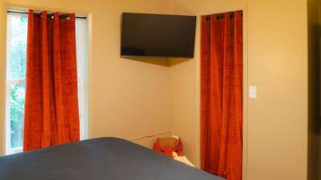 A room with a bed, a flat-screen TV mounted on the wall, and a window with red curtains.