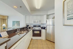 A compact kitchen with white cabinets, a microwave, a stove, and a refrigerator. - Carolinian Beach Resort 1036 (Myrtle Beach)