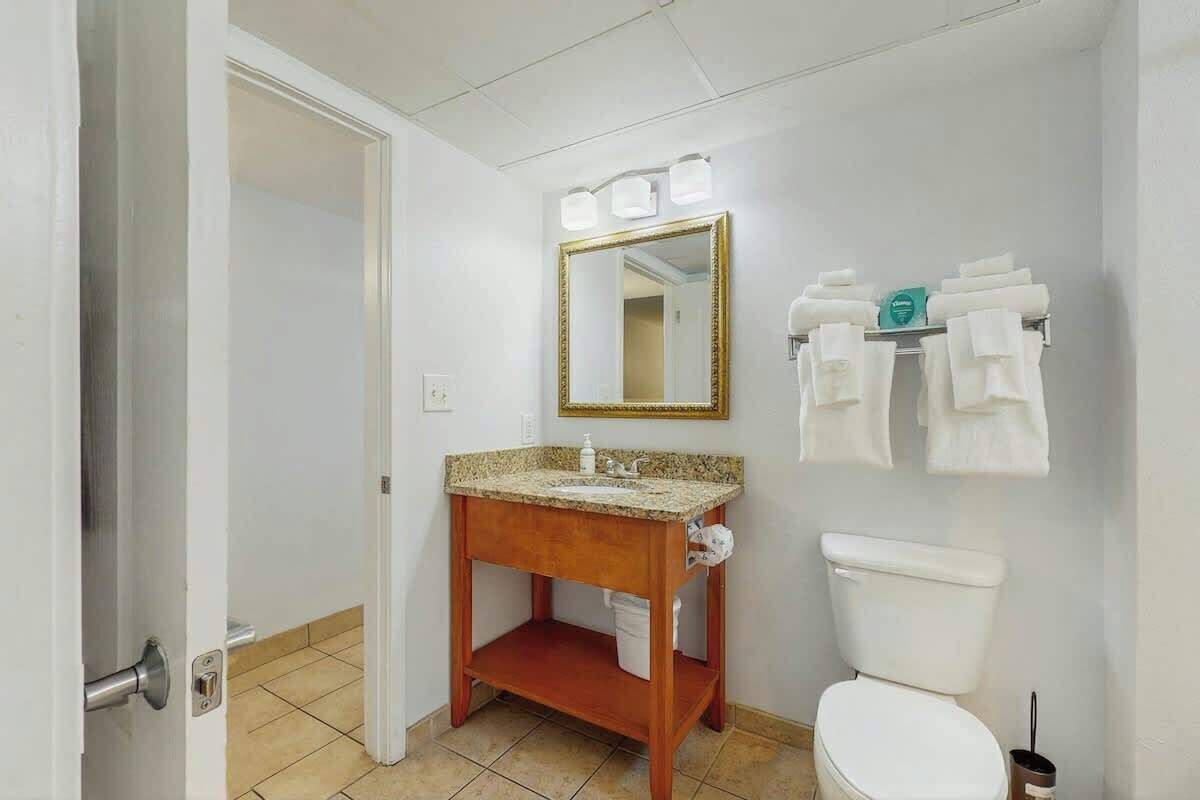 A bathroom with a wooden vanity, a sink, a toilet, and a mirror with lights.