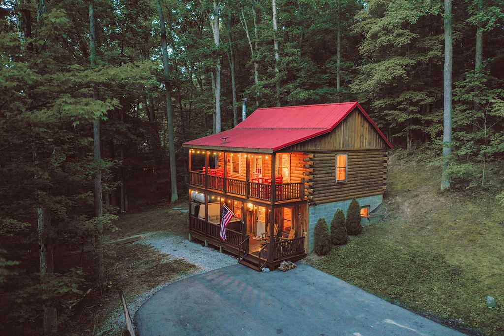 Una cabaña de madera con techo rojo, balcón y porche iluminado con guirnaldas de luces.