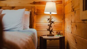 A wooden cabin room with a bed, a nightstand with a lamp, and a small decorative item. - Scarlet Fox | Hocking Hills, Hot Tub, Firepit (Logan)