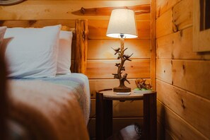 Ein Zimmer in einer Holzhütte mit einem Bett, einem Nachttisch mit Lampe und einem kleinen dekorativen Gegenstand.