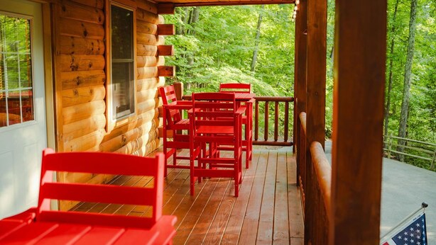 A wooden cabin with a porch, red chairs, and a view of a forest. - Scarlet Fox | Hocking Hills, Hot Tub, Firepit (Logan)