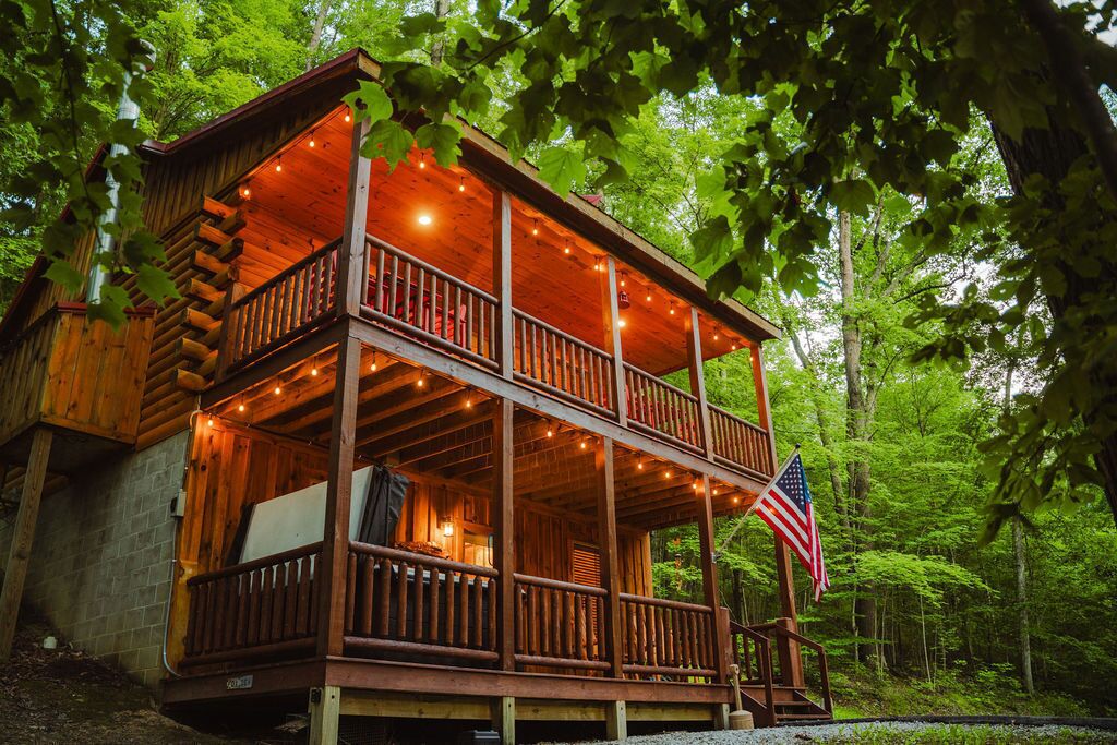 A two-story log cabin with a balcony, surrounded by trees.