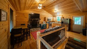 A wooden cabin interior with a dining area, kitchen, and a fireplace. - Scarlet Fox | Hocking Hills, Hot Tub, Firepit (Logan)