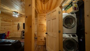 A wooden interior with a laundry area, a bed, and a red chair. - Scarlet Fox | Hocking Hills, Hot Tub, Firepit (Logan)