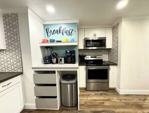 A modern kitchen with white cabinetry, a built-in microwave, a stainless steel oven, and a coffee maker on the countertop.