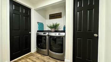 A laundry room with two front-loading washers and dryers, a sign above them, and a potted plant on top of the dryers.