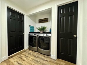 A laundry room with two front-loading washers and dryers, a sign above them, and a potted plant on top of the dryers.