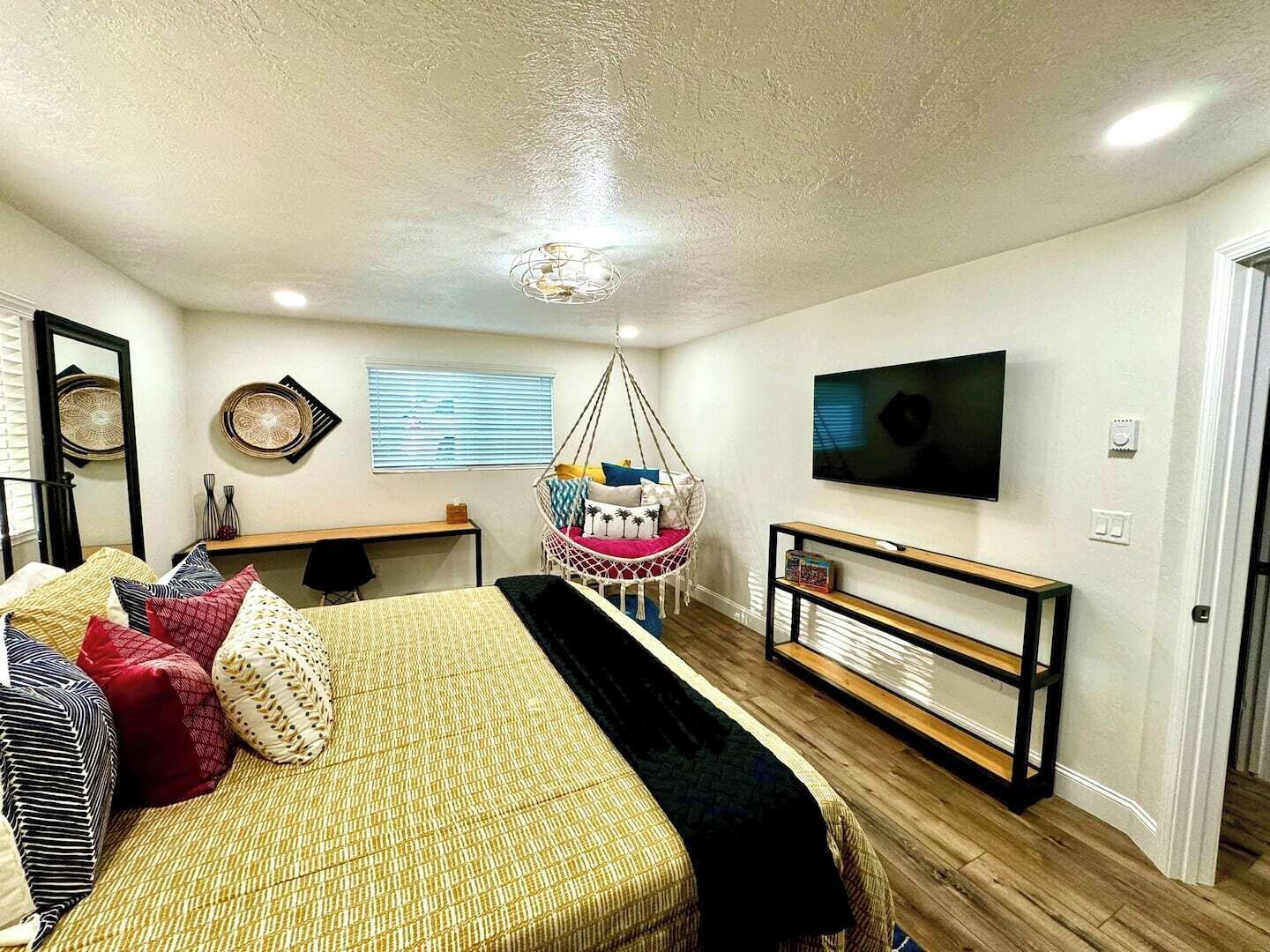 A bedroom with a bed, a hanging chair, a TV, and a desk.