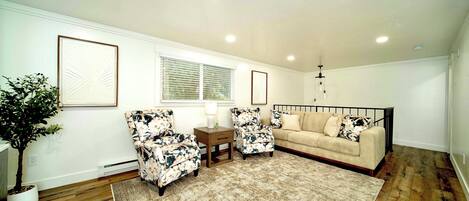Una sala de estar con un sofá color crema, dos sillones con estampado floral, una mesa de centro y una planta grande en maceta.
