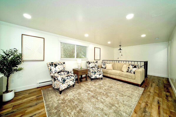 A living room with a beige sofa, two floral armchairs, a coffee table, and a large potted plant.