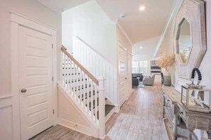 A hallway with white doors, a wooden staircase, and a dining area with a table and chairs. - Lux Family Beach Retreat | Pool Slide • Hot Tub (Hilton Head Island)