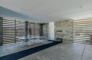 A spacious indoor area with a ping pong table, a door, and a wall-mounted coat rack. - Lux Family Beach Retreat | Pool Slide • Hot Tub (Hilton Head Island)
