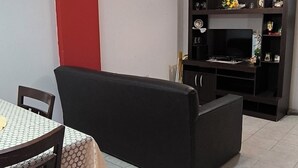 A dining area with a table and chairs, a black sofa, and a TV stand with shelves.