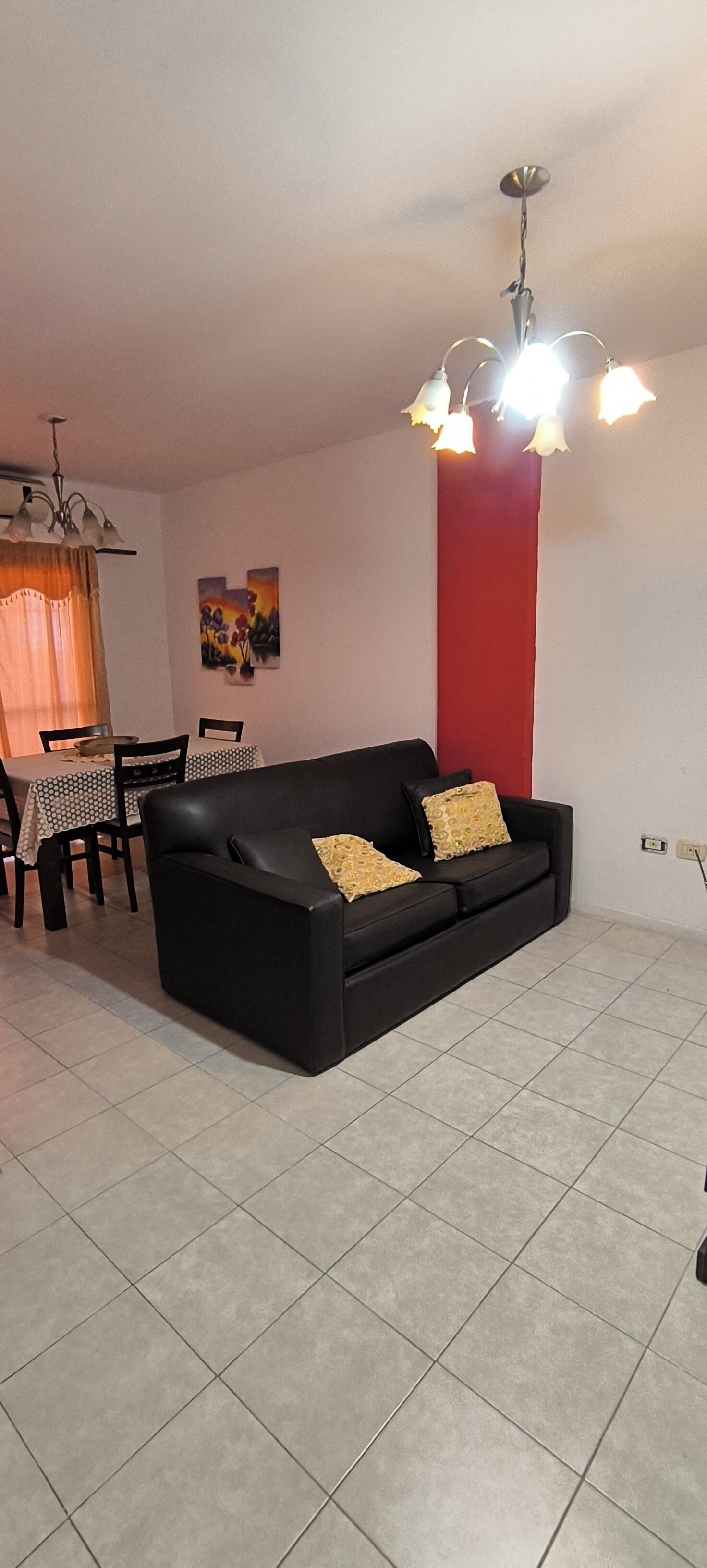 Un salon avec un canapé noir, une table à manger avec des chaises et un mur d’accent rouge.