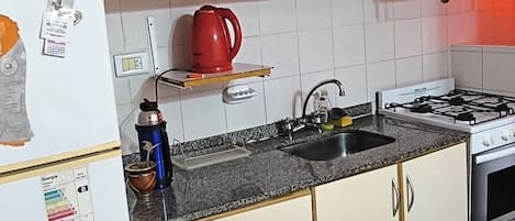 A kitchen with white cabinets, a red kettle, a stove, and a refrigerator.