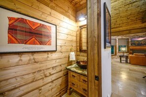 A wooden interior with a framed textile, a sink with a bowl, and a wooden door leading to a living area. - The Guesthouse: Romantic luxury retreat for two with forest views & a soaker tub (Broken Bow)