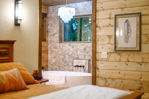 Ein Schlafzimmer mit einem großen Bett, einem Fenster, einer Badewanne und einer Holzwand.