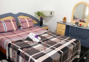 Ein Hotelzimmer mit Bett, Nachttisch, Kommode, Spiegel und einer kleinen Pflanze.
