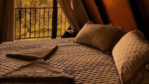 A bedroom with a sloped ceiling, a bed with pillows, and a view of trees through a window. - Chalé da Lagoa (Cordilheira Alta)
