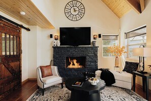 Ein Wohnzimmer mit Kamin aus Stein, einer Wanduhr und einem Fernseher darüber.