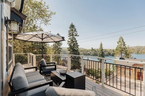 Une terrasse dotée de mobilier d’extérieur, d’une table et d’un parasol, offrant une vue sur un lac bordé d’arbres et sur une rive éloignée.