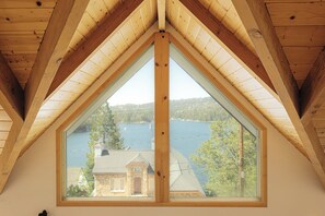 A room with a large triangular window offering a view of a body of water and buildings. - Palisades & Pine - Lake Views • Game Rm • Fire Pit (Lake Arrowhead)